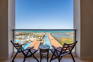 Un balcon avec deux chaises en bois et une petite table, donnant sur un complexe hôtelier doté d’une piscine, de toboggans aquatiques et d’une plage.