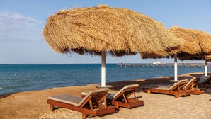 A beach with wooden lounge chairs and thatched umbrellas. - SUNRISE Solara Aqua park Resort (Hurghada)