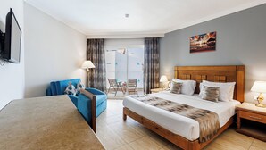 A hotel room with a bed, a desk, a blue sofa, and a view of the outdoors through a glass door. - SUNRISE Solara Aqua park Resort (Hurghada)