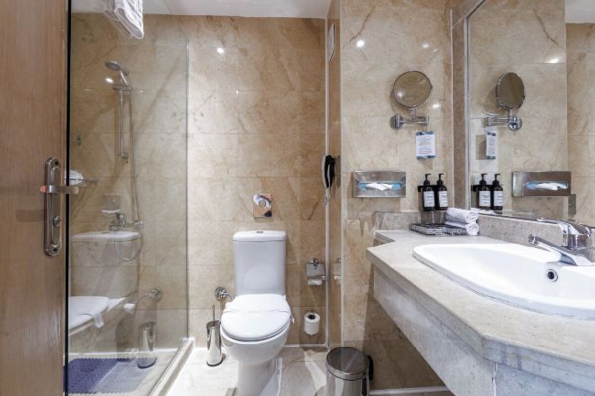 Une salle de bain moderne avec une douche à parois de verre, des toilettes blanches, un grand lavabo avec un miroir et des articles de toilette posés sur le comptoir.