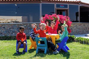 Children sitting at a table outdoors with a stone wall and a building in the background. - SUNRISE Solara Aqua park Resort (Hurghada)