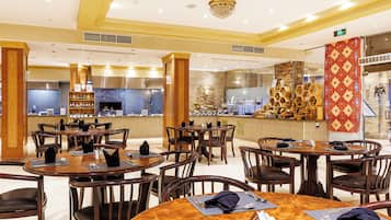 A restaurant with round tables, wooden chairs, and a kitchen area in the background.