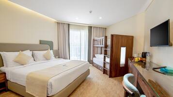 A hotel room with a large bed, a desk with a chair, a TV, and a bunk bed.