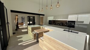 Une cuisine moderne dotée d’un îlot central, d’appareils électroménagers intégrés et de luminaires suspendus.