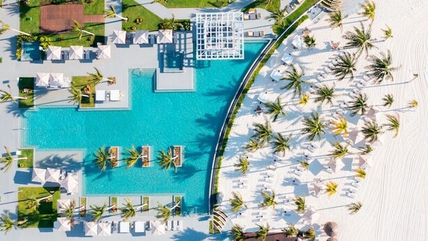 Vista aérea de un resort con piscina, tumbonas y palmeras.
