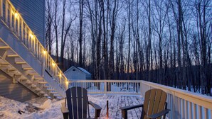 A wooden deck with Adirondack chairs and a fire pit, surrounded by snow and trees. - 3-Bedroom 2 Bath Cozy Chalet 1 Mile From Mountain! (Lanesville)