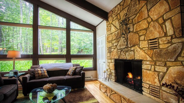 A cozy living room with a stone fireplace, large windows, and a comfortable seating area. - 3-Bedroom 2 Bath Cozy Chalet 1 Mile From Mountain! (Lanesville)