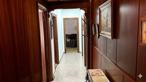 Un couloir aux murs lambrissés, doté d’un sol carrelé et d’une porte donnant sur un salon avec un canapé.