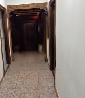 Un pasillo estrecho con puertas de madera y suelo de baldosas.