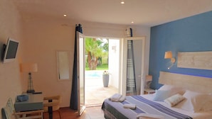 Un dormitorio con cama, escritorio, silla, televisor y vistas al exterior.