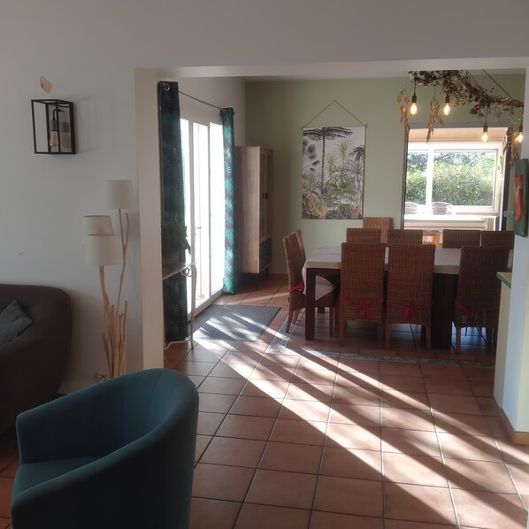 Uma área de refeições com mesa e cadeiras, um sofá e uma janela grande com vista para o verde.