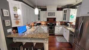 A modern kitchen with a central island, bar stools, stainless steel appliances, and white cabinetry. - Peach Jam Luxury Gentleman's Retreat ~ 5 BR BA One of a kind find! (North Augusta)