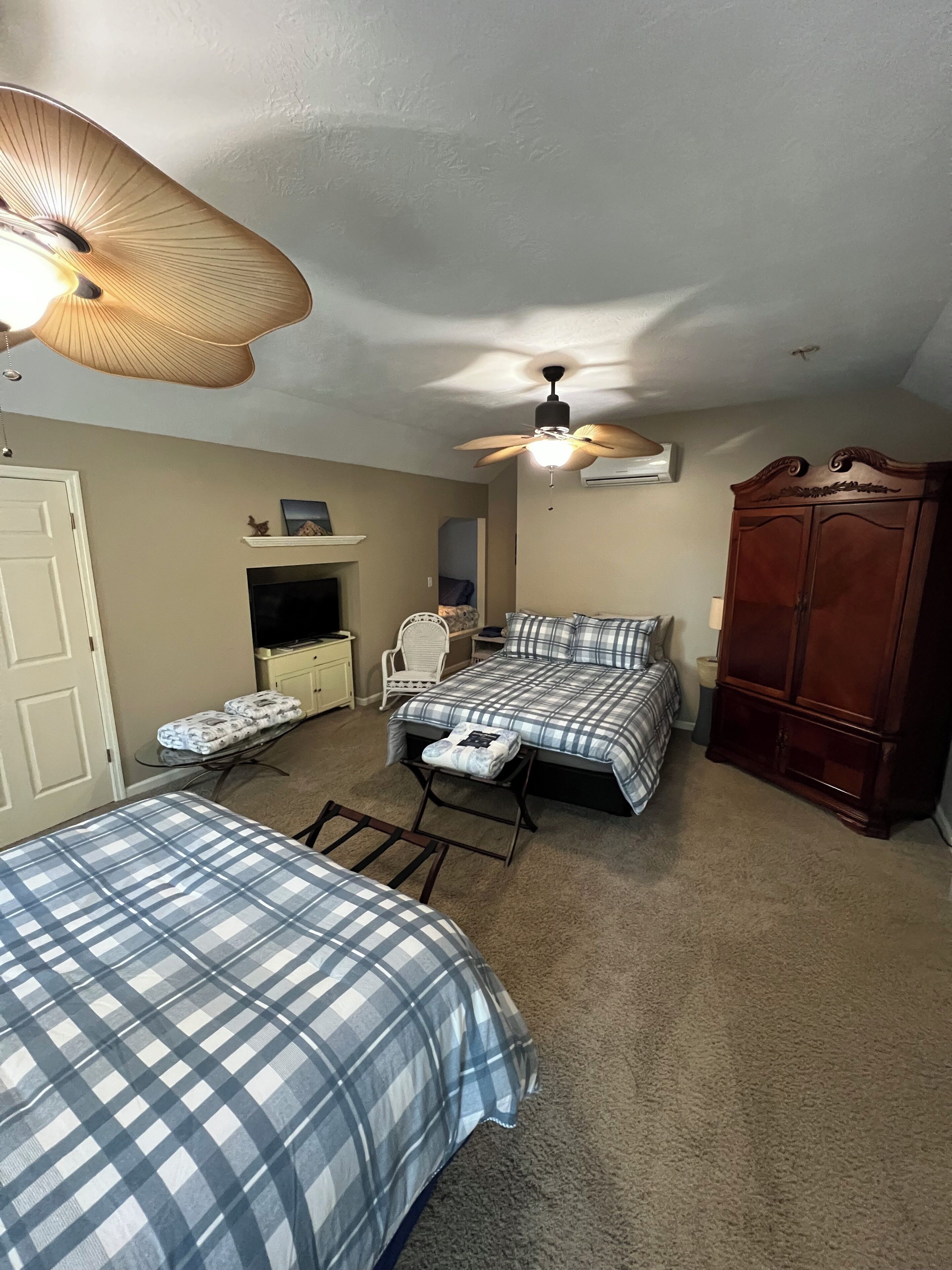A bedroom with two beds, a ceiling fan, a wardrobe, and a small table with a chair.