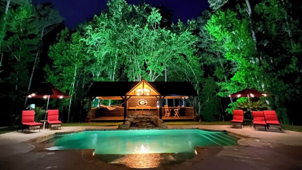 A nighttime view of a lodge with a swimming pool, red lounge chairs, and a wooden cabin structure. - Peach Jam Luxury Gentleman's Retreat ~ 5 BR BA One of a kind find! (North Augusta)