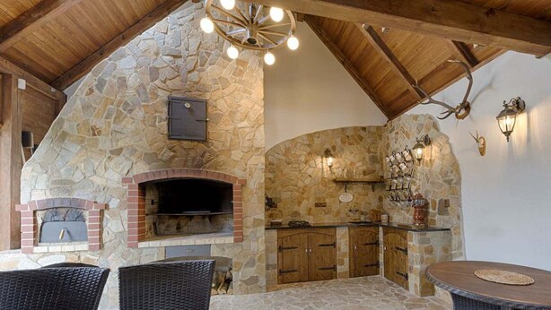 An outdoor kitchen with stone walls, a brick oven, and a dining area with wicker furniture. - Chalet in Liberec Near Ski Resort Jested (Svetla pod Jestedem)