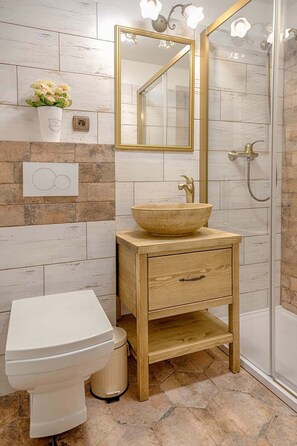 Ein Badezimmer mit einem Holzwaschtisch, einem weißen Waschbecken, einem spiegel mit goldener Rahmung und einer Duschkabine.
