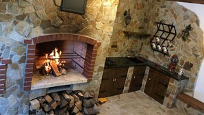 A stone fireplace with a fire, a stone wall, and a small kitchen area with a sink and cabinets. - Chalet in Liberec Near Ski Resort Jested (Svetla pod Jestedem)
