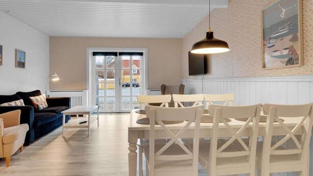 A modern living room with a dining area, featuring a large window, a sofa, a table, and chairs. - 5 Star Holiday Home in Lokken (Lokken)
