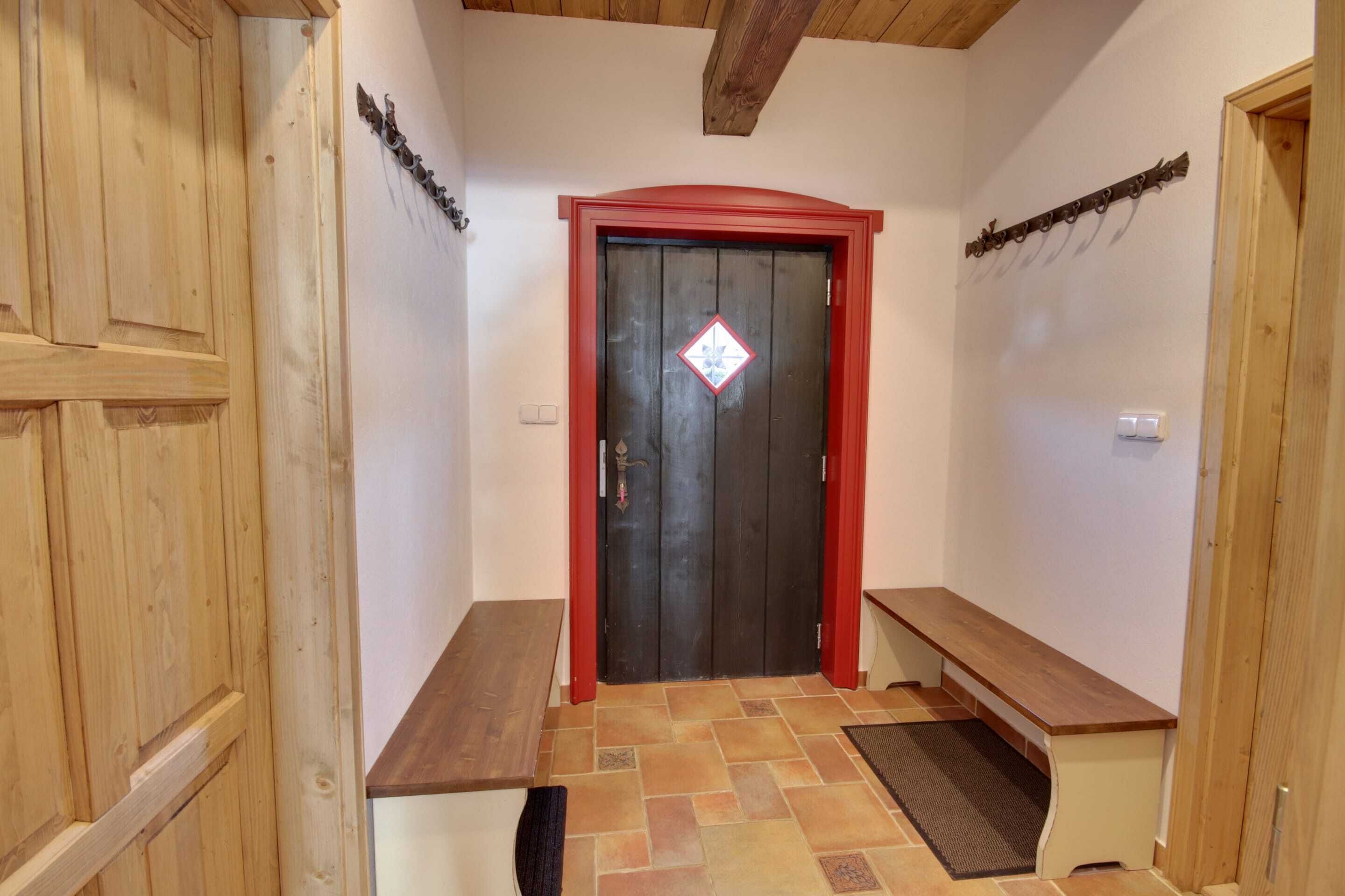 A hallway with a wooden bench, a red-framed door, and a tiled floor.
