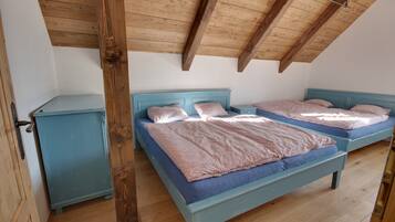 A bedroom with two beds, wooden beams on the ceiling, and a small cabinet.