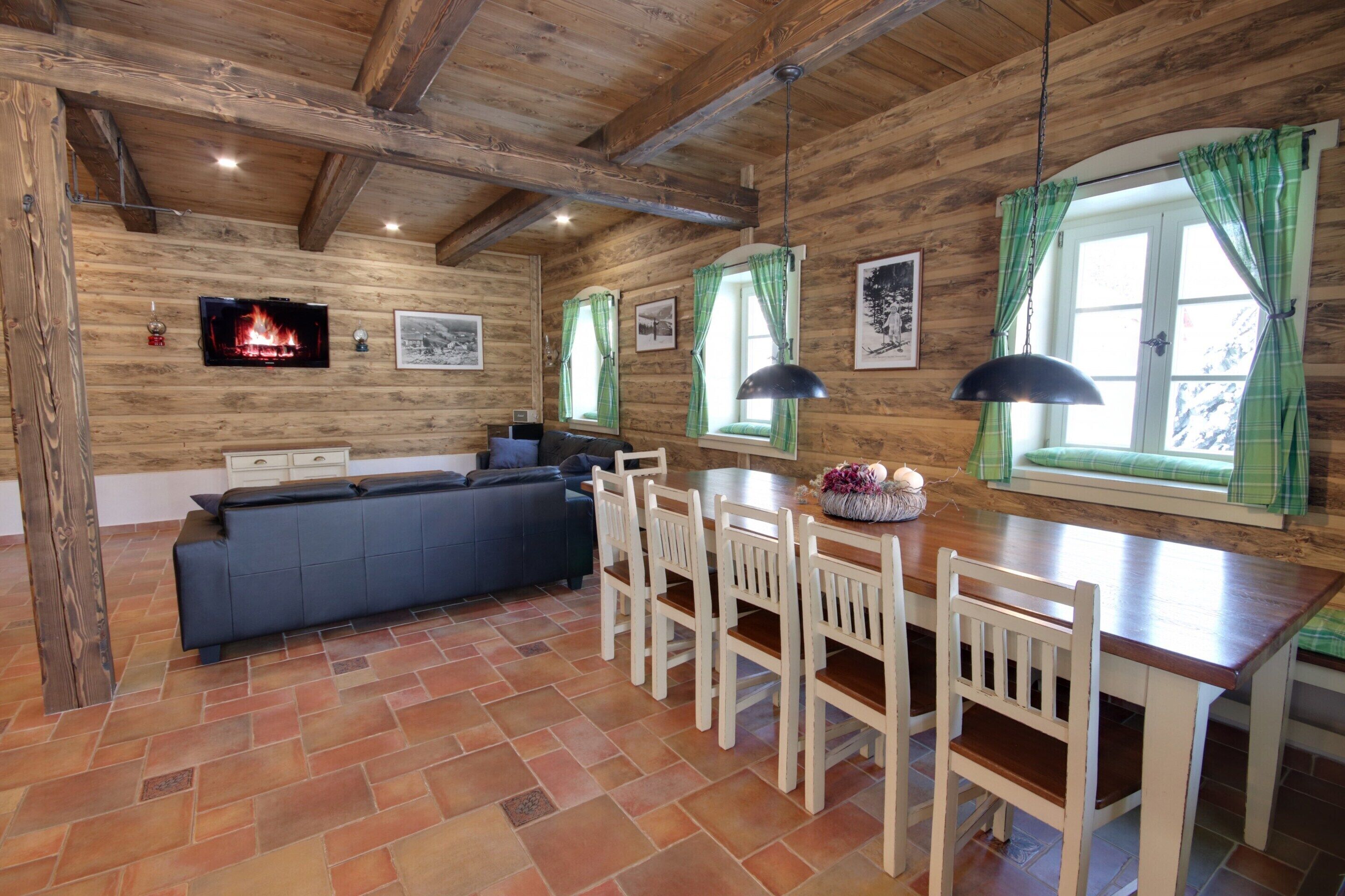 A rustic wooden interior with a fireplace, a sofa, dining table, chairs, and a television.