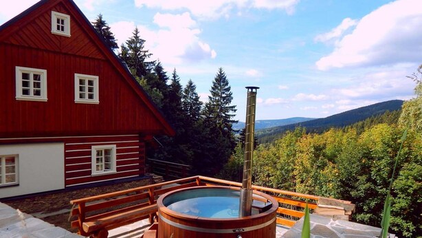 A wooden hot tub with stone steps, a red cabin, and a forested mountain backdrop. - Villa Near Horni Domky Ski Resort (Rokytnice nad Jizerou)