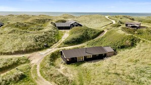 Een afgelegen, grasachtig landschap met meerdere houten huisjes, verbonden door onverharde paden, met uitzicht op een uitgestrekt wateroppervlak.