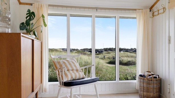 Een kamer met een schommelstoel, een groot raam met uitzicht op een grasveld, een houten kast en een rieten mand.