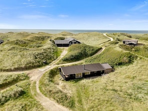 Una propiedad costera con varias edificaciones rodeadas de dunas, con un sendero de tierra que las conecta.