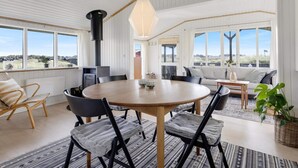 Een ruime kamer met een ronde houten tafel, zwarte stoelen en een groot raam met uitzicht op de omgeving.
