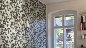 Een woonkamer met een bank, een salontafel en een stoel. Er is een raam met uitzicht op een huis en een hek.