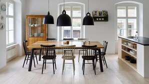 Een eethoek met een houten tafel en stoelen, zwarte hanglampen en een houten kast met servies.