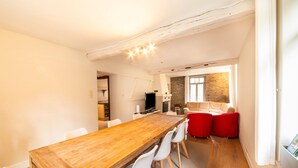 A spacious dining area with a wooden table and white chairs, a kitchen with stone walls, and a living area with red sofas. - Historic Watermill in Bohan (Vresse-sur-Semois)