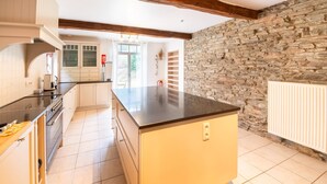 A kitchen with a central island, white cabinets, a stone wall, and a tiled floor. - Historic Watermill in Bohan (Vresse-sur-Semois)