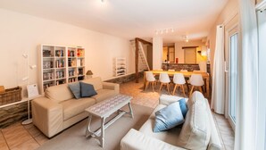 A living room with a sofa, a coffee table, and a bookshelf. There is a dining area with a table and chairs. - Historic Watermill in Bohan (Vresse-sur-Semois)