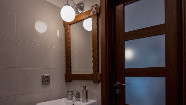 A bathroom with a white sink, a mirror, and a wooden door with frosted glass panels. - Villa in Ore Mountains Near Ski Areal Kliny (Klíny)