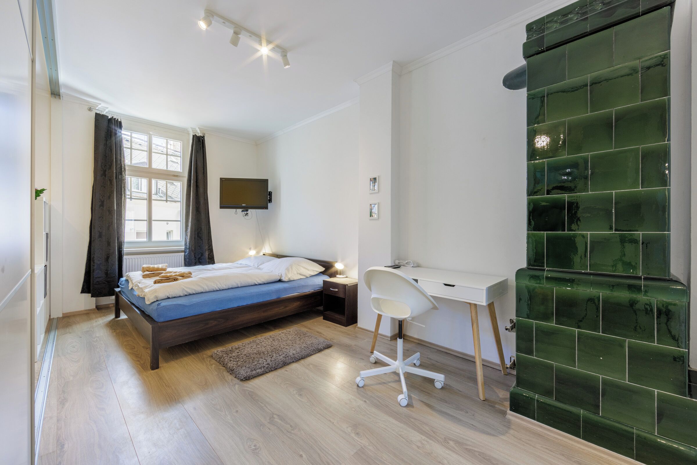 A bedroom with a bed, bedside table, desk, chair, and a green tiled wall.