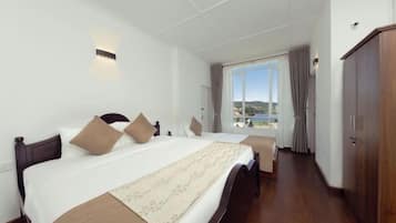 A hotel room with a large bed, a wooden wardrobe, and a window with a view.