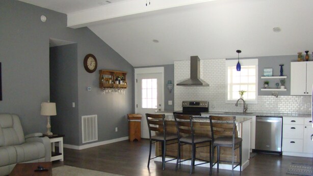 A spacious living room with a sofa, a coffee table, and a dining area with chairs. A kitchen with a stove, sink, and cabinets is visible in the background. - Charming 2 bedroom home in Tallassee, Alabama near Lake Martin (Tallassee)