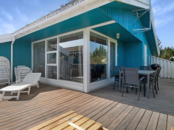 A covered outdoor deck with a dining area, lounge chairs, and a large sliding glass door leading to a patio. - 5 Star Holiday Home in Blokhus (Blokhus)