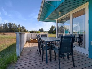 A wooden deck with a table and chairs, overlooking a grassy field and trees. - 5 Star Holiday Home in Blokhus (Blokhus)