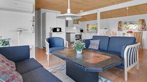 A modern living space with a central island table, a sofa, and a dining area with chairs. - 5 Star Holiday Home in Blokhus (Blokhus)
