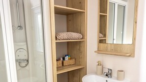 A bathroom with a glass-enclosed shower, a white pedestal sink, wooden shelves with baskets, and a mirror.