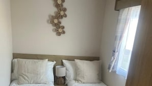 A hotel room with two single beds, a small bedside table with a lamp, a decorative wall piece, and a window with curtains.