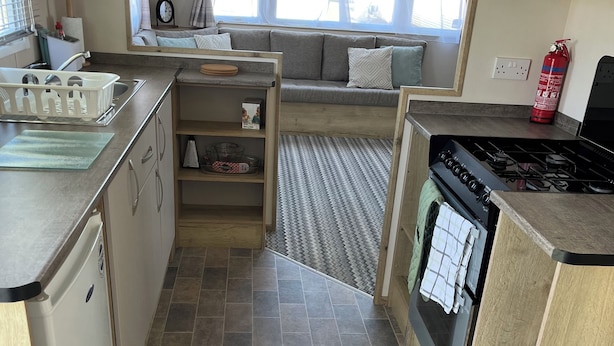A compact kitchen with a stove, sink, and a small refrigerator. There is a window with curtains, a sofa, and a rug.