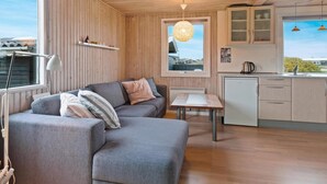 A modern cabin interior with a grey sofa, wooden walls, a small kitchen, and a window with a view. - 5 Star Holiday Home in Lokken (Lokken)