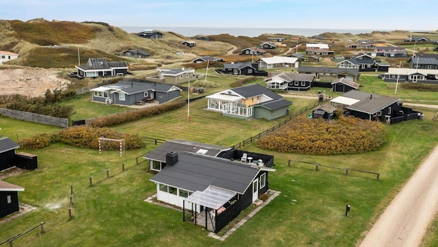 An aerial view of a coastal housing development with multiple houses, some with attached garages, and a clear view of the sea in the background. - 5 Star Holiday Home in Lokken (Lokken)