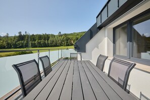 Parvekkeella on puinen pöytä ja tuolit, ja sieltä avautuu näkymä vehreään maisemaan.