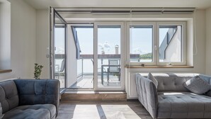Ett modernt vardagsrum med en grå soffa, en till grå soffa och ett stort fönster med utsikt över himlen och bergen.