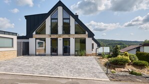 Ett modernt hus i två våningar med en stor uppfart och utsikt över det omgivande landskapet.